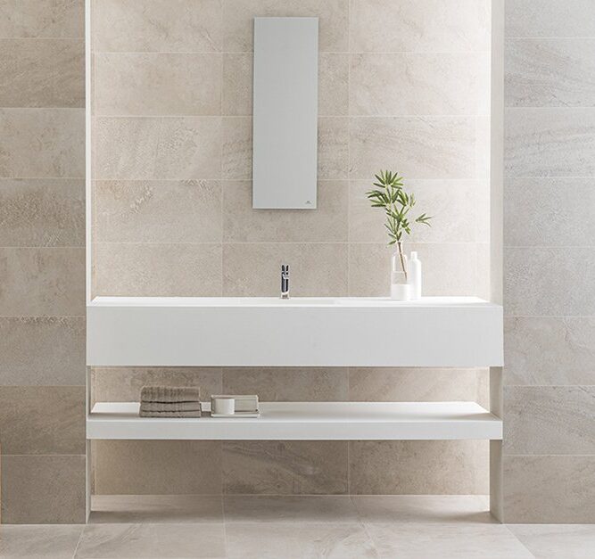 Minimalist bathroom with large beige stone tiles, a sleek white floating vanity, open shelf storage, and simple décor including a vase with greenery.