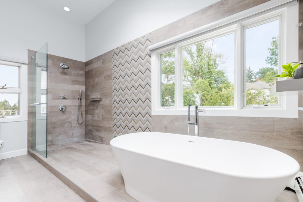 Contemporary bathroom with a freestanding soaking tub, curbless walk-in shower, textured accent tile wall, and large windows bringing in natural light.