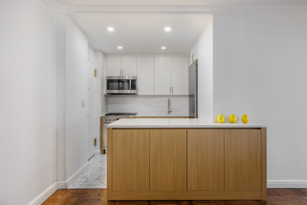 Minimalist kitchen with white cabinetry, light wood island, stainless steel appliances, marble backsplash, and three decorative yellow objects on the counter