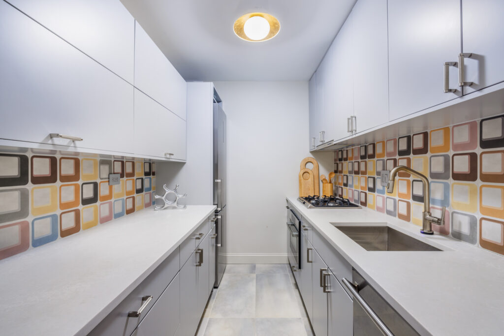 Modern galley kitchen with white cabinetry, quartz countertops, and colorful square-patterned tile backsplash
