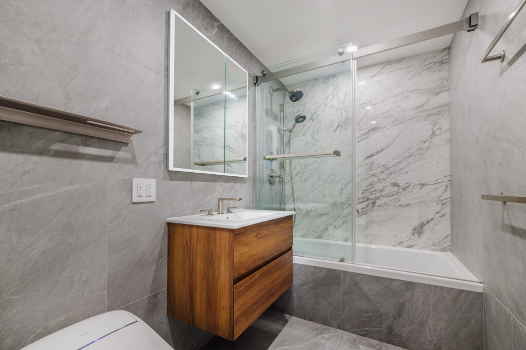 Compact urban bathroom design with a minimalist floating vanity, large illuminated mirror, and spa-inspired marble shower surround.