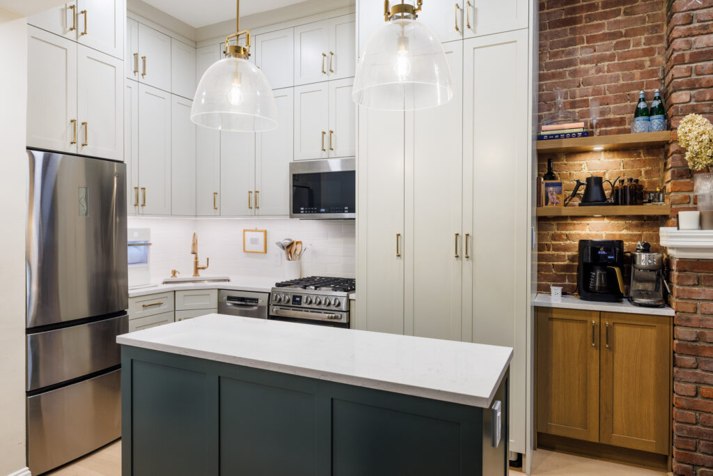 Transitional kitchen with white cabinetry, stainless steel appliances, a small island, exposed brick wall, and built-in coffee station with wood accents