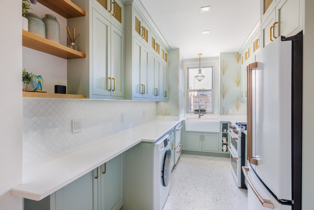 Galley kitchen with sage green cabinetry, white countertops, farmhouse sink, patterned wallpaper, open shelving, and a window with city views