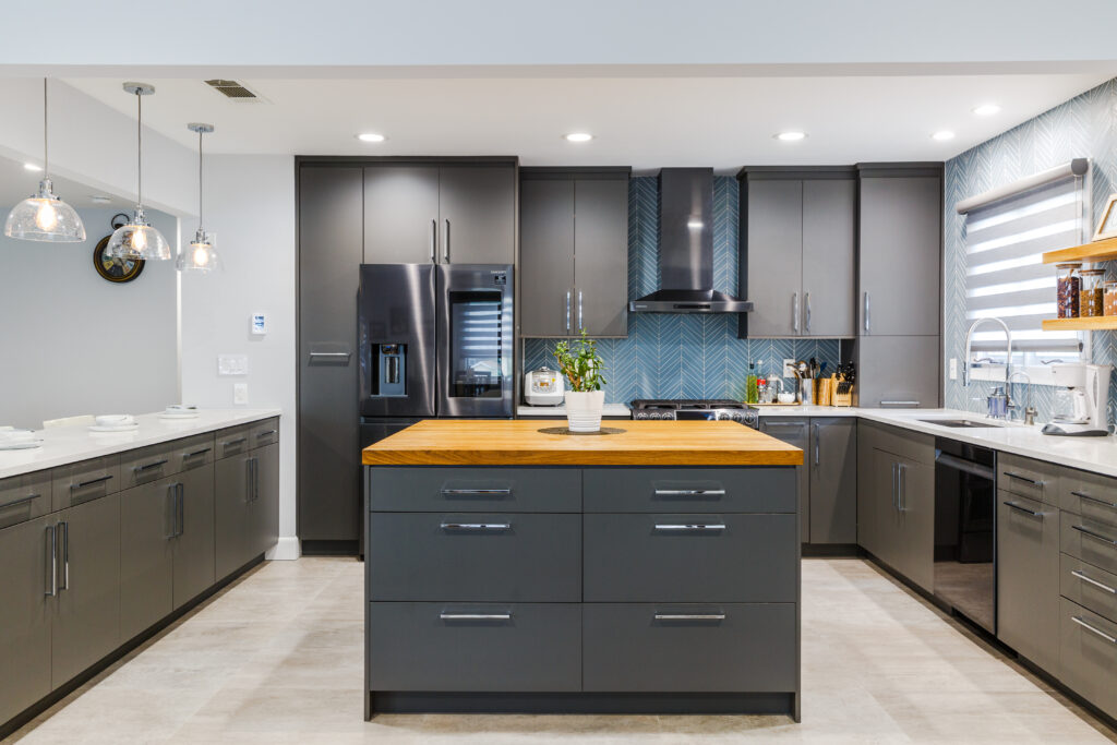 Modern kitchen with dark gray cabinets, wood island countertop, stainless steel appliances, and pendant lighting