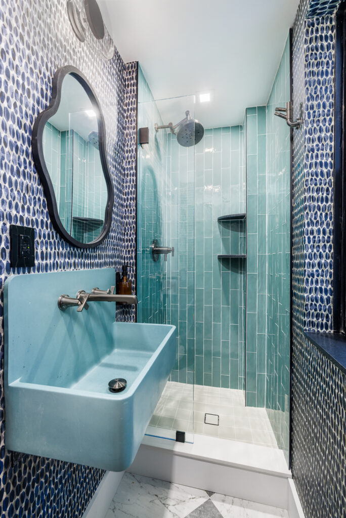 Vibrant Manhattan bathroom remodel featuring bold blue mosaic wall tiles, a modern floating sink, and a glass-enclosed shower with aqua subway tiles for a striking contemporary look.