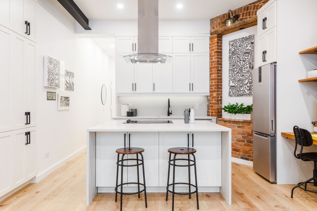 Stylish Manhattan kitchen remodel blending industrial charm with modern design, featuring exposed brick, sleek white cabinetry, and a waterfall-edge island with bar seating.