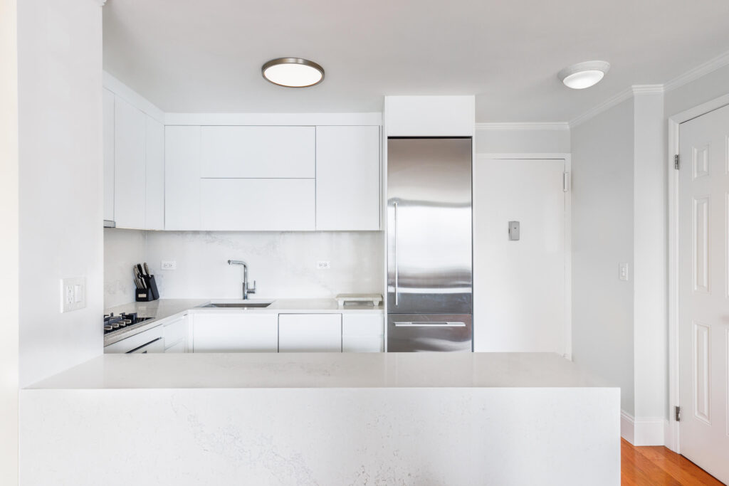 Minimalist Manhattan kitchen renovation featuring flat-panel white cabinetry, integrated appliances, and a seamless marble-look backsplash for a crisp, modern finish.