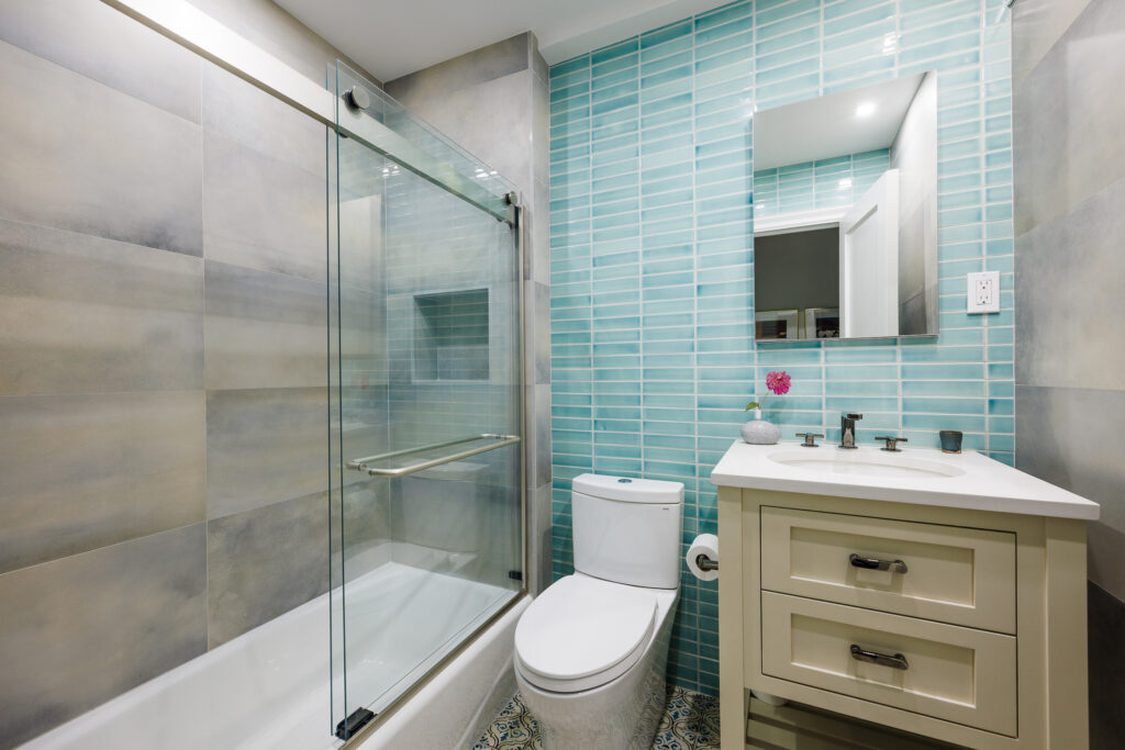 Modern Manhattan bathroom remodel featuring aqua blue subway tile walls, a frameless glass tub enclosure, and a compact vanity for stylish city living.