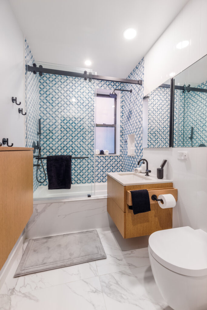 Bright bathroom design with bold geometric wall tiles, floating vanity, and a glass-enclosed tub-shower combo for urban living.