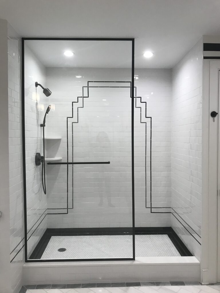 Spacious glass-enclosed shower featuring striking black geometric tile accents on crisp white walls for an Art Deco-inspired design.