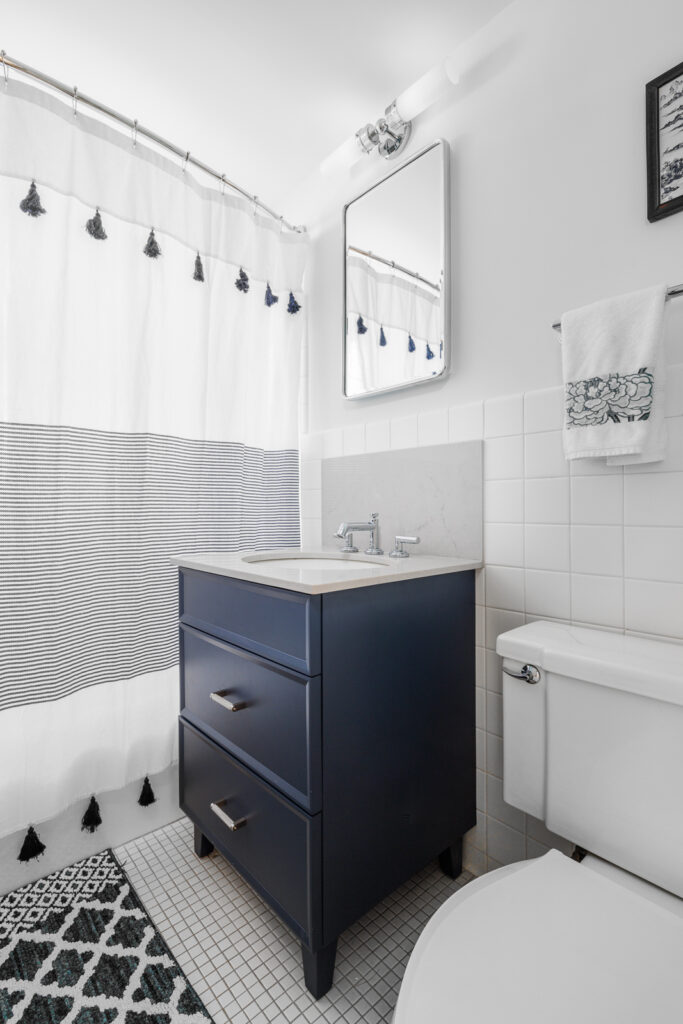 Manhattan bathroom remodel featuring a navy blue vanity, patterned shower curtain, and white tiled walls for a fresh, modern look.