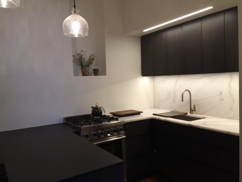 Close-up angle of a contemporary NYC kitchen with integrated lighting, pendant glass fixtures, and a bold black-and-white palette anchored by warm wood floors.