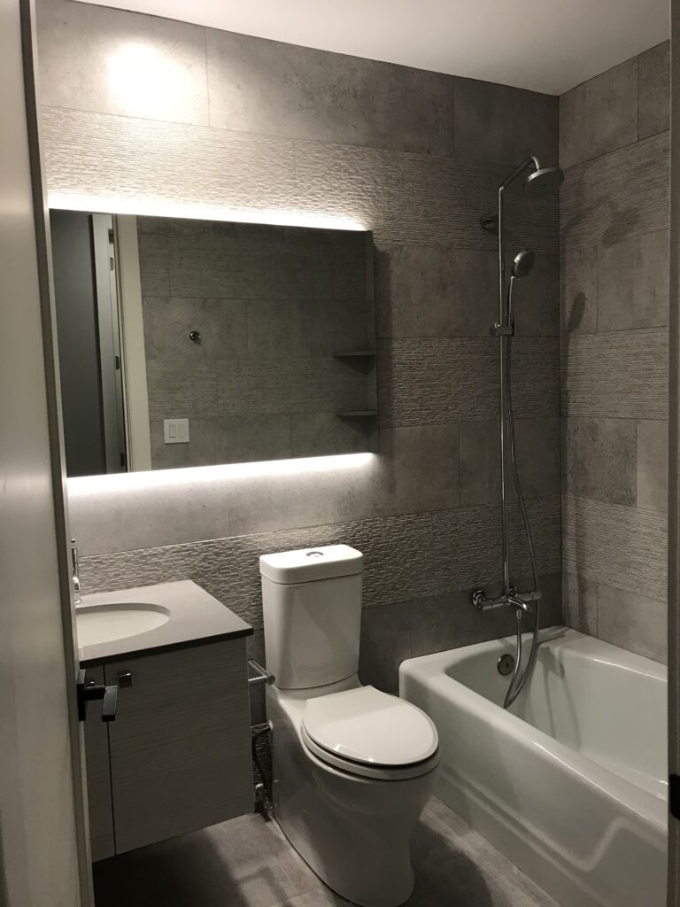 Modern Manhattan bathroom remodel featuring a sleek tub-shower combo, floating vanity, and full-wall mirror with LED backlighting.
