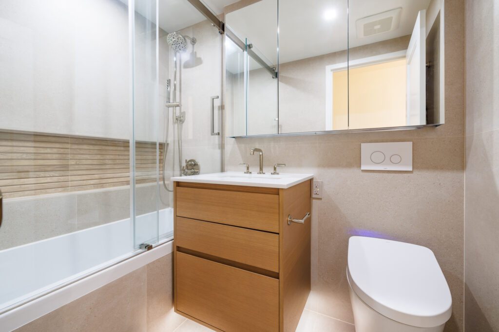 Modern Manhattan bathroom remodel with a sleek wood vanity, glass-enclosed tub-shower, and warm neutral tile accents.