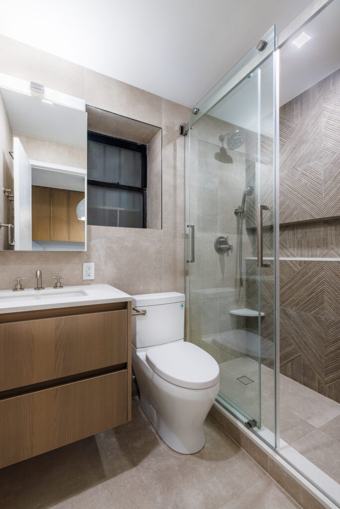 Contemporary Manhattan bathroom remodel featuring a glass-enclosed shower, sleek wood vanity, and neutral tile design that maximizes space and light.