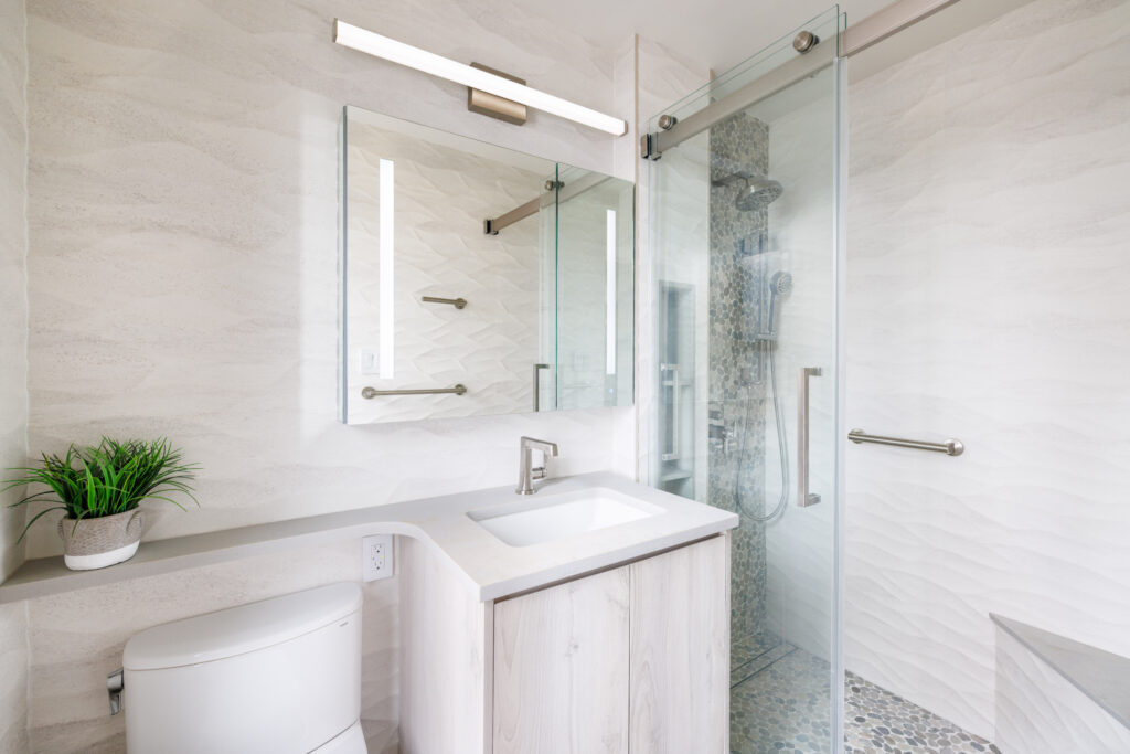 Modern bathroom renovation by D2 Design & Works featuring custom vanity, glass-enclosed walk-in shower, textured tile walls, and minimalist fixtures in a NYC apartment.
