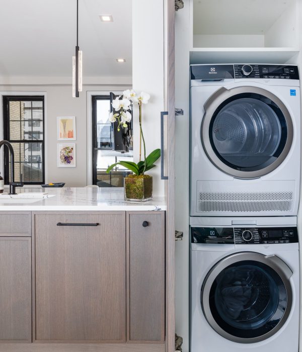 Home remodeling contractor in West Village. Modern laundry area featuring a stacked Electrolux washer and dryer set within a white cabinet beside a light wood kitchen counter topped with white marble.