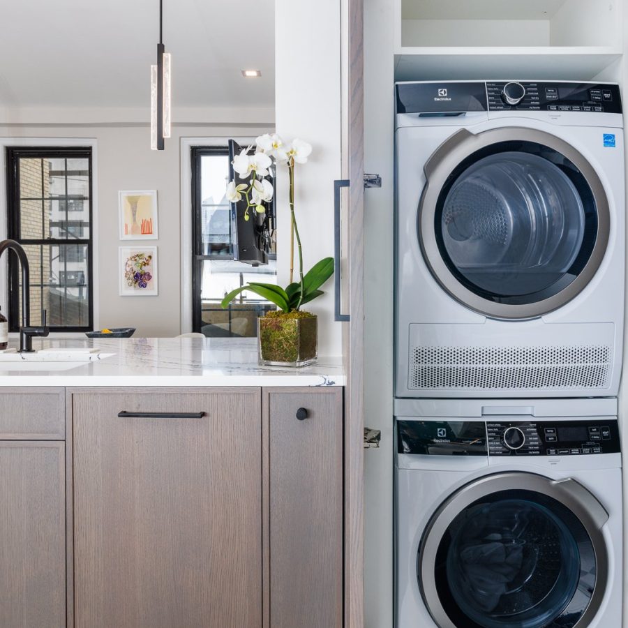 Home remodeling contractor in West Village. Modern laundry area featuring a stacked Electrolux washer and dryer set within a white cabinet beside a light wood kitchen counter topped with white marble.