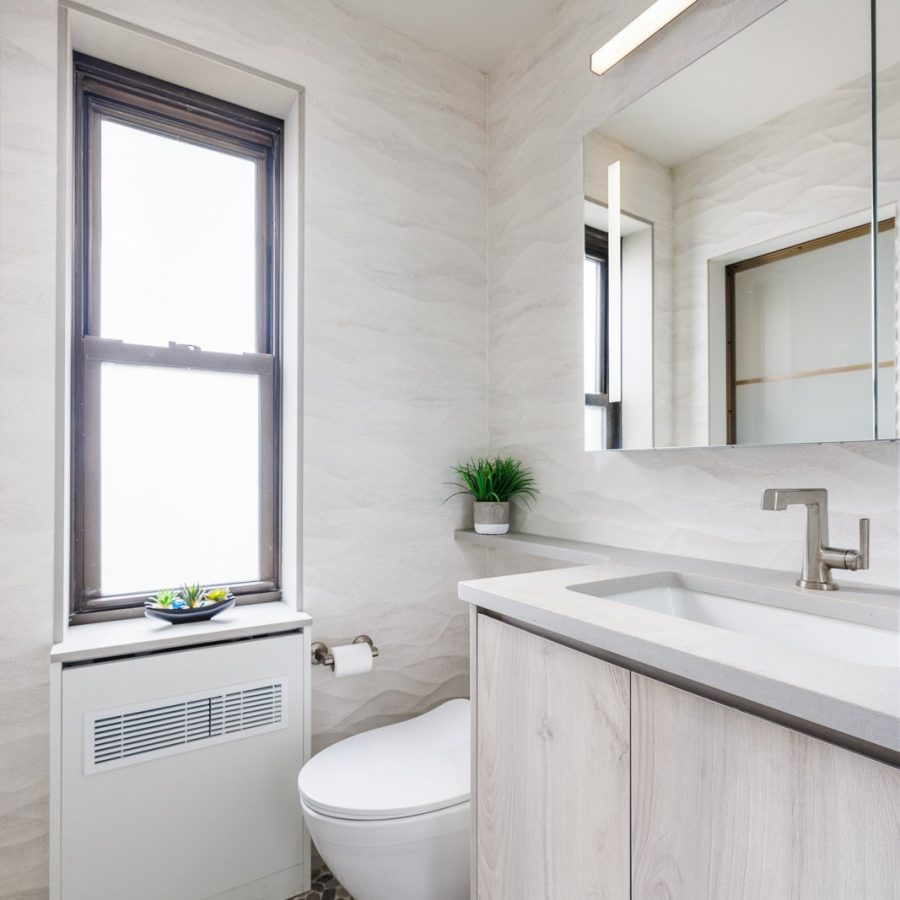 09234 Bright modern bathroom with light wood cabinetry, a large mirror, and a window letting in natural light above a white toilet.