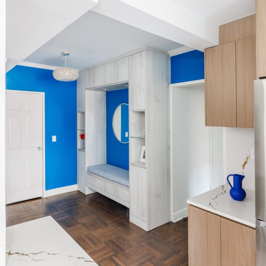 10106 Bright modern entryway featuring bold cobalt blue accent walls paired with white ceilings and marble flooring. A built-in bench with wood panel details and recessed shelving adds functionality, while warm wood cabinetry on the side introduces natural texture. The design creates a vibrant yet clean aesthetic with striking color contrast. Apartment renovation in Manhattan.