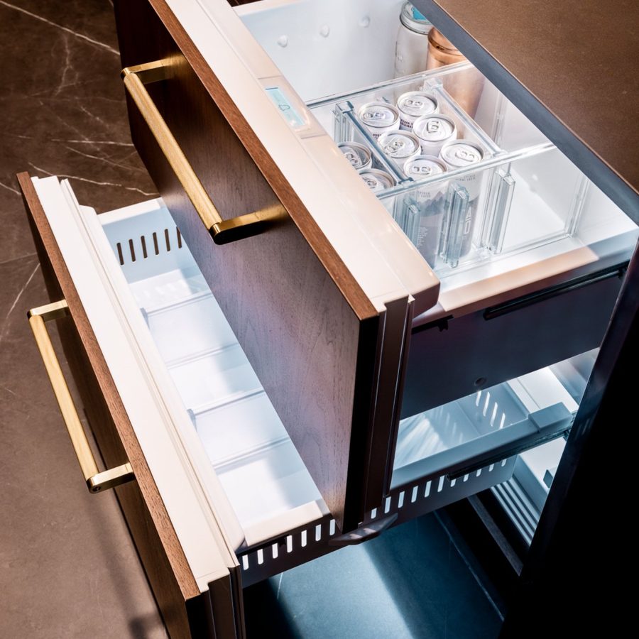10152 Home remodeling contractor in Turtle Bay. Close-up view of a luxury built-in drawer-style refrigerator with wooden panel fronts, brass handles, and organized beverage storage inside the top drawer.
