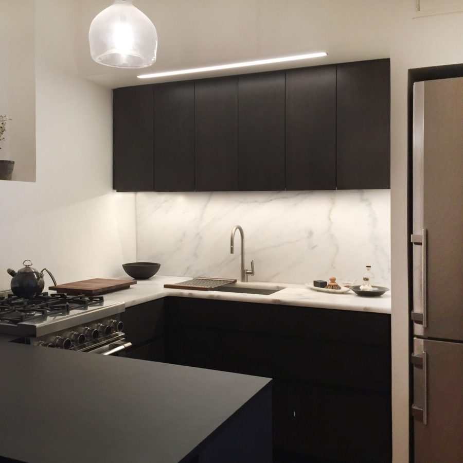 10174 Sleek modern kitchen with dark cabinetry, marble backsplash and countertops, under-cabinet lighting, stainless steel appliances, and a minimalist pendant light.