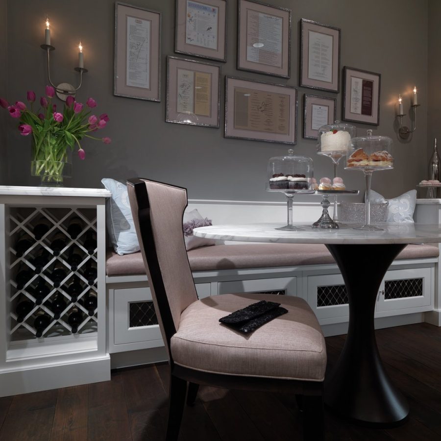 02034 Elegant dining nook with a round marble table, upholstered chair, built-in bench seating, wall-mounted candle sconces, framed certificates, and a wine rack cabinet.