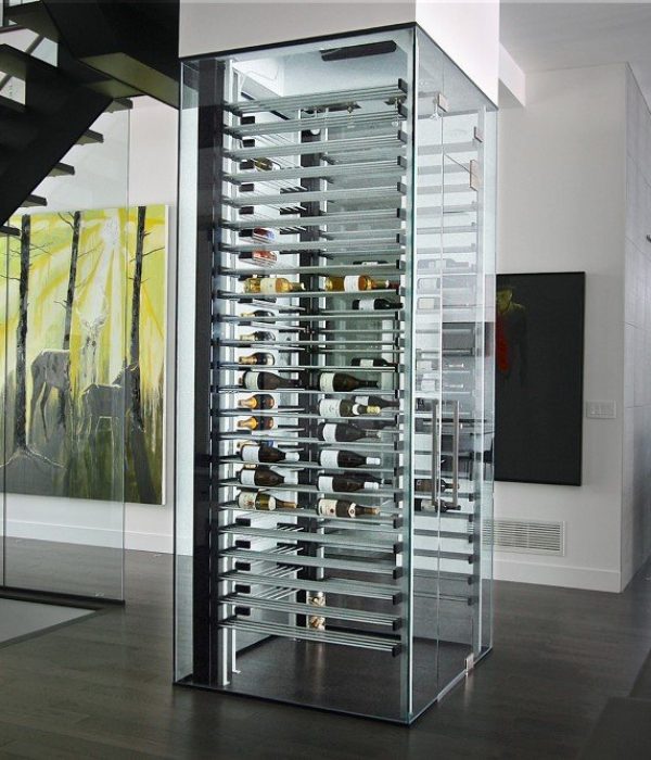 Contemporary living space featuring a glass-enclosed wine tower with horizontal metal racks, adjacent to a modern floating staircase and large abstract forest artwork.