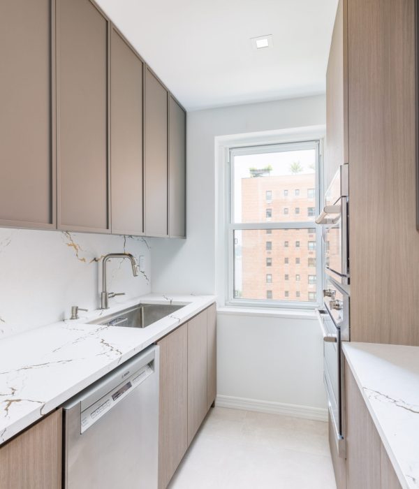 Light-filled kitchen with full-height wood cabinetry, white countertops, and a marble backsplash. A large window provides natural light, while the clean design highlights soft neutrals and efficient use of space.