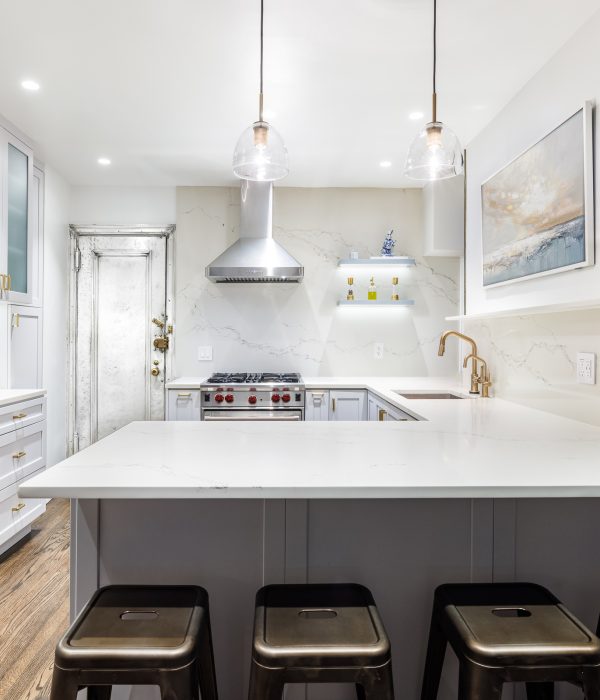 Modern kitchen with a large white island featuring seating for three, pendant lighting overhead, and gray lower cabinetry. A blend of stainless steel appliances and soft-toned finishes creates a welcoming open-concept space.