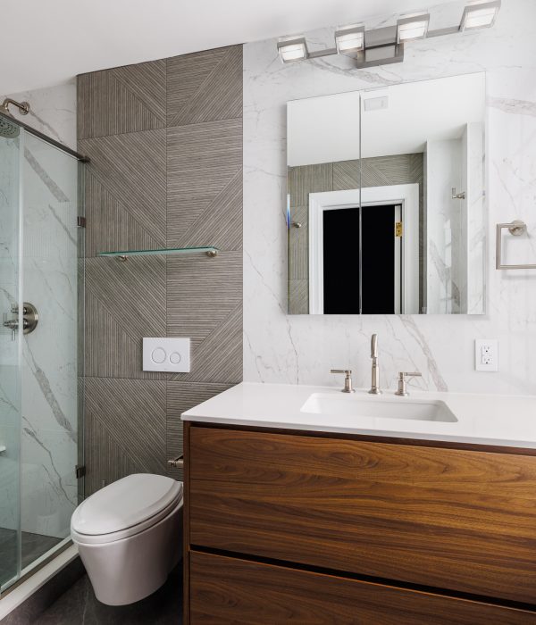 Contemporary bathroom with a light wood floating vanity, white countertop, and frameless mirror. The design features subtle beige walls, a glass shower enclosure, and a minimalist approach to maximize small space functionality.