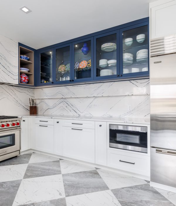 Elegant kitchen with striking navy blue upper cabinets paired with white marble backsplash and countertops. The space includes a professional gas range, open shelving, and checkered marble flooring for a bold, upscale look.