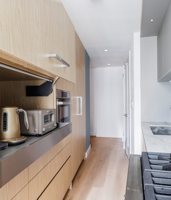 Contemporary kitchen featuring white upper cabinets and wood-tone lower cabinetry, paired with a stainless steel refrigerator and range. A simple pendant light and white backsplash complete the modern design.