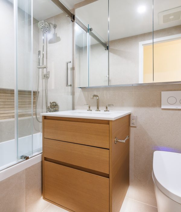 Bright bathroom featuring a pair of light wood vanities, frameless mirrors, and a glass shower enclosure. Neutral walls and soft lighting create a cohesive, modern look ideal for maximizing functionality in compact spaces.