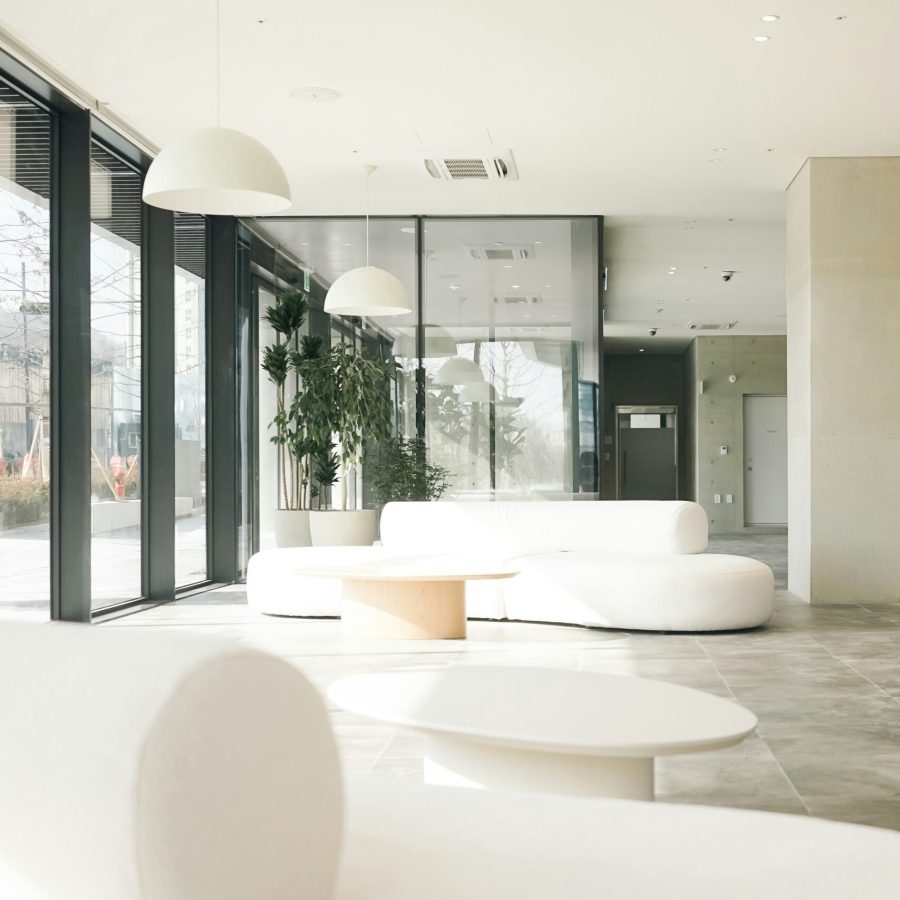 jiran-family-gK9t2kYr-g8-unsplash (1) Home remodeling contractor in Uptown. Bright, modern lobby with large floor-to-ceiling windows, minimalist white furniture, pendant lighting, and indoor plants in a sleek, open space.